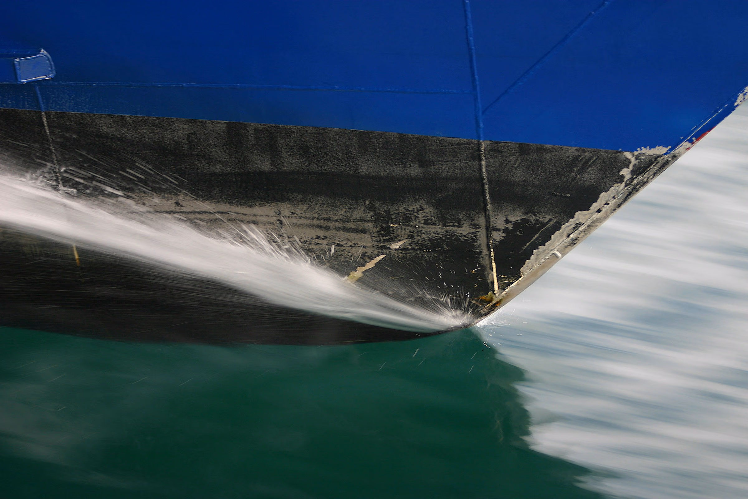 Close-up of a blue and black boat hull cutting rapidly through green water, creating splashing spray.