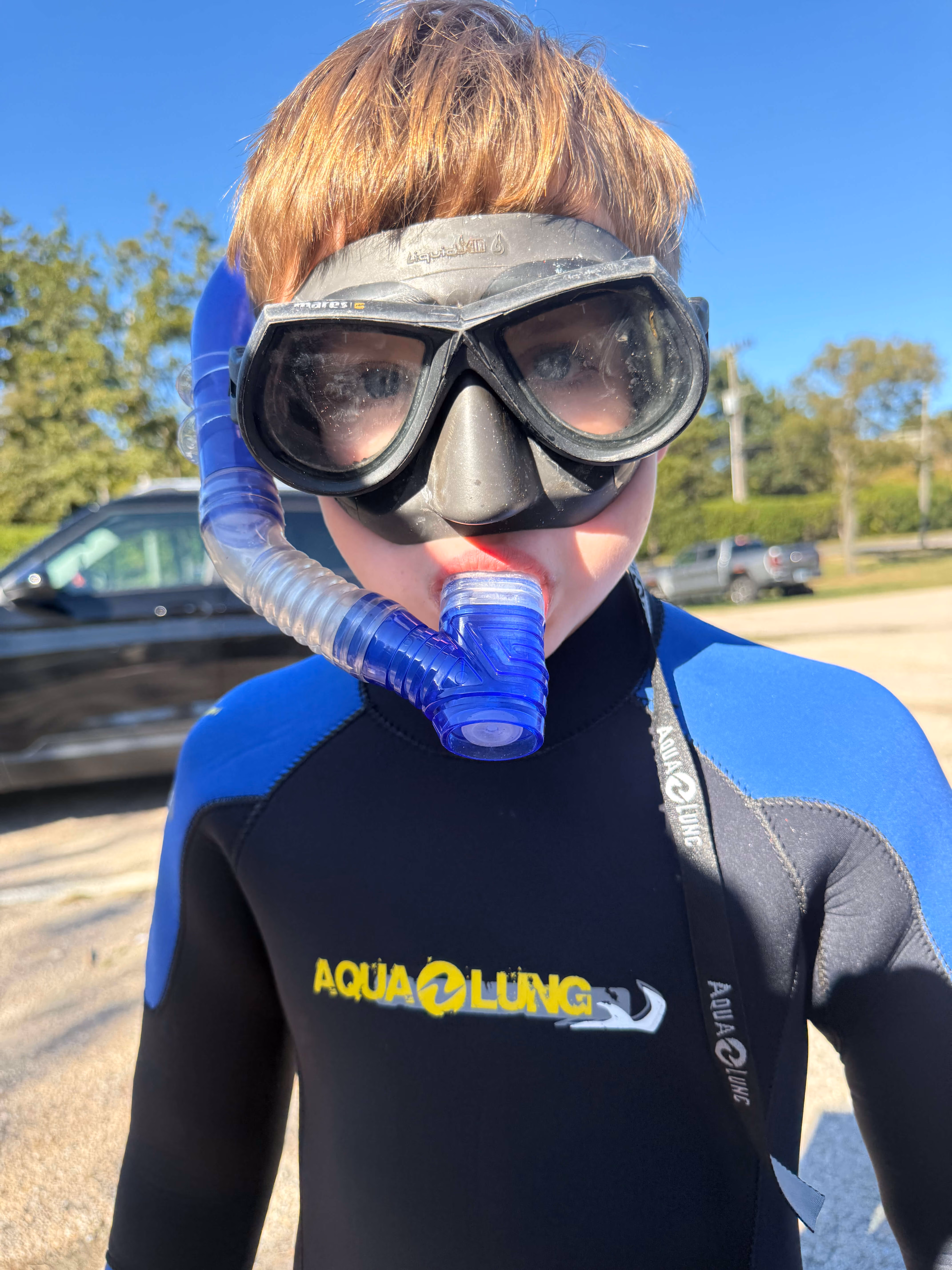 Child wearing black and blue wetsuit with Aqua Lung logo and snorkel mask with a blue snorkel tube.