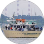 White and orange ferry boat named L.C. Lake Charles on water near city buildings and trees.