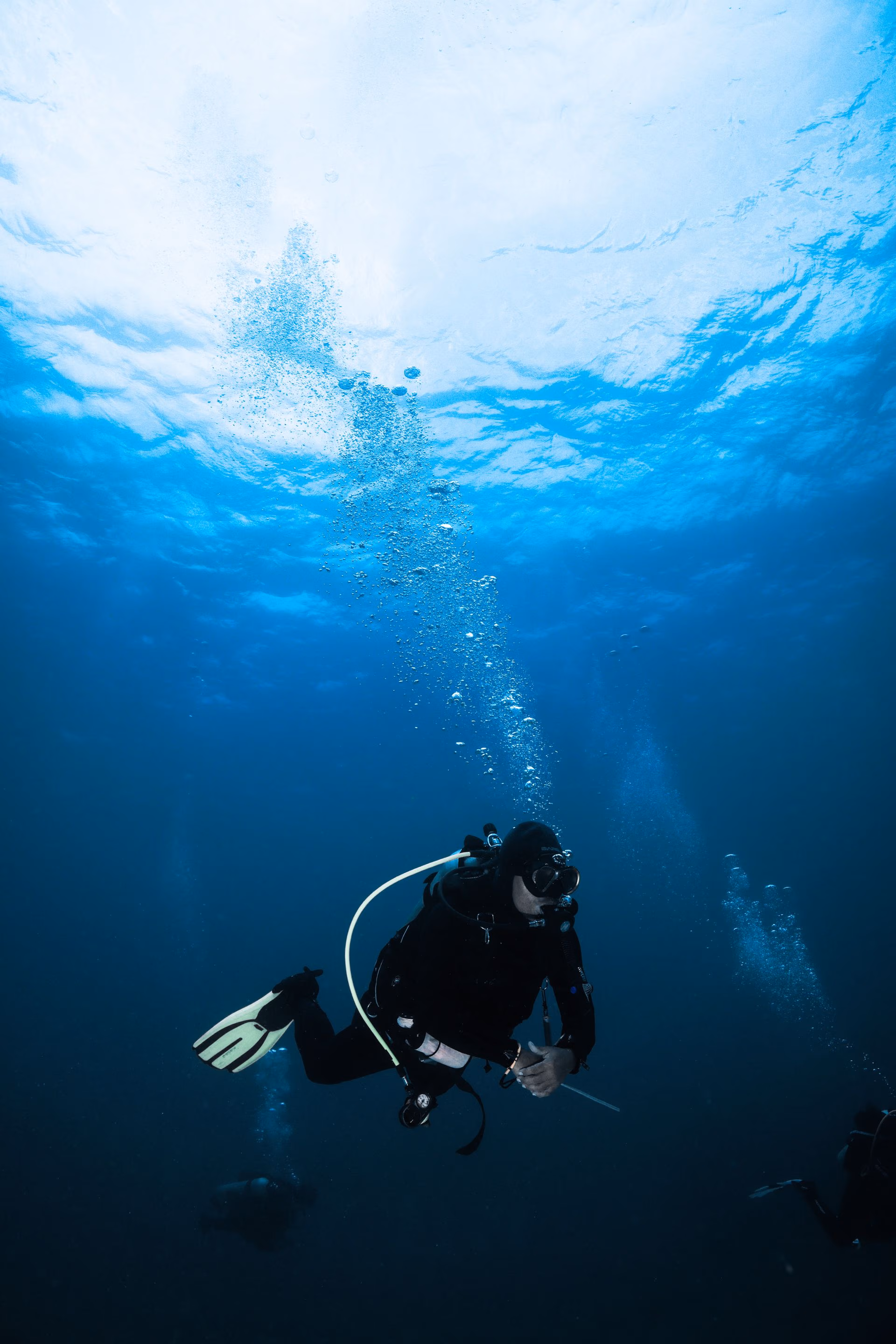 Scuba diver underwater wearing black gear and yellow fins with bubbles rising toward the surface.